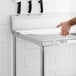 A hand uses a knife to cut on a white poly top table with a backsplash.