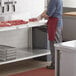 A man cutting meat on a Regency stainless steel poly top table in a professional kitchen.