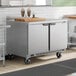 A stainless steel 48-inch dual temperature worktop refrigerator and freezer unit with two doors and casters.