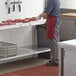 A man in a red apron and gloves cutting meat on a Regency poly top work table in a kitchen.