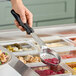 A hand using a Vollrath black Perforated Oval Spoodle to serve food at a salad bar.