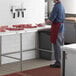 A man in a red apron cutting meat on a Regency poly top work table.