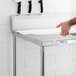 A person cutting on a Regency stainless steel poly top table with a white poly top.