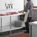 A man in a butcher shop wearing an apron cutting meat on a Regency poly top table with a backsplash and undershelf.