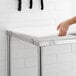 A hand touching a white poly top on a Regency stainless steel work table.