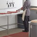 A man cutting meat on a Regency stainless steel poly top table.