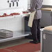 A man in a kitchen wearing an apron stands at a Regency stainless steel poly top table with a knife on the counter.