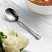 An Acopa stainless steel bouillon spoon in a bowl of soup.