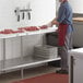 A man in a red apron and gloves cutting meat on a Regency stainless steel poly top table.