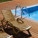 A Lancaster Table & Seating sand resin chaise lounge on a pool deck.