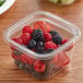 A plastic container of berries with a Fabri-Kal LSQ TruWare Square Plug Fit PET Deli Lid on a table.