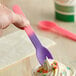 A hand holding a pink and purple color-changing heavy weight plastic spoon over a cup of ice cream.