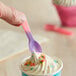 A hand holding a pink to purple color-changing tasting spoon over a cup of ice cream.