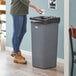 A woman standing next to a Lavex gray rectangular trash can.