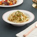 A Visions white plastic bowl filled with pasta and a spoon and fork on a napkin.