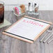 A natural wood menu board with a menu on a table.