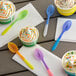 Assorted color-changing plastic spoons in blue, yellow, orange, purple, and pink on a white napkin.