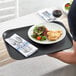 A person holding a Choice black non-skid serving tray with a plate of food, silverware, and a glass of red wine.