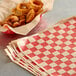 A basket of fried onion rings next to red and white checkered deli wrap paper.