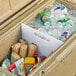 A CaterGator divider in a cooler filled with food and drinks on a table outdoors.