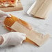 A hand holding a sandwich in a Kraft paper bag with a window.