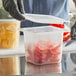 A person in black gloves holding a San Jamar translucent plastic food container with food in it.