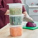 A person cutting vegetables in a San Jamar translucent plastic food pan on a counter.