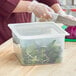 A woman cutting green leaves in a San Jamar translucent plastic food pan on a counter.