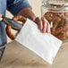 A hand using a knife to cut a pretzel over a white sandwich bag.