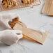 A hand in a white glove holding a Kraft paper bag with a window and pastries inside.