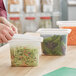 A person's hand putting shredded cabbage and carrots in a San Jamar translucent plastic food container.