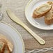 A Visions gold plastic knife on a plate with a piece of bread and butter.