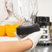 A person in gloves uses a Waring repair kit to fix a Waring blender on a counter in a smoothie shop.