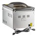 A stainless steel tabletop vacuum packaging machine with a clear domed lid and power cord.