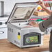 A woman using an ARY VacMaster tabletop vacuum packaging machine on a counter.