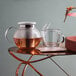 A Villeroy & Boch glass teapot with a clear container and white lid on a table with a glass cup and saucer.