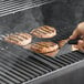 A person cooks a hamburger on a Backyard Pro wood-fired pellet grill.