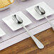 A group of white plates with stainless steel scoop spoons on them.