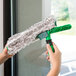 A hand holding a green and white Unger ErgoTec Ninja window cleaning tool.