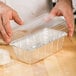 A hand holding a clear plastic container of dough.