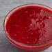 A bowl of Les Vergers Boiron red raspberry puree on a table with a spoon.