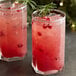 Two glasses of pink pomegranate drinks with red berries and rosemary sprigs.