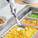 A hand in a glove holding a gray Vollrath Spoodle over macaroni and cheese.