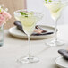Two Acopa Covella margarita glasses filled with margaritas and garnished with lime slices on a table.