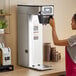 A woman using a Bunn BrewWISE stainless steel coffee maker on a counter in a coffee shop.