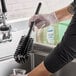 A person in rubber gloves using a Carlisle black bottle cleaning brush over a sink.