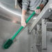 A person in gloves cleaning a stainless steel tank with a Carlisle green brush with a green handle.