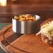 A Soho brushed stainless steel ramekin filled with food on a wood table.