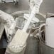 A gloved hand uses a Carlisle white multi-purpose cleaning brush to clean a glass.