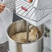 A person in a white coat using an Estella spiral dough mixer to mix dough.